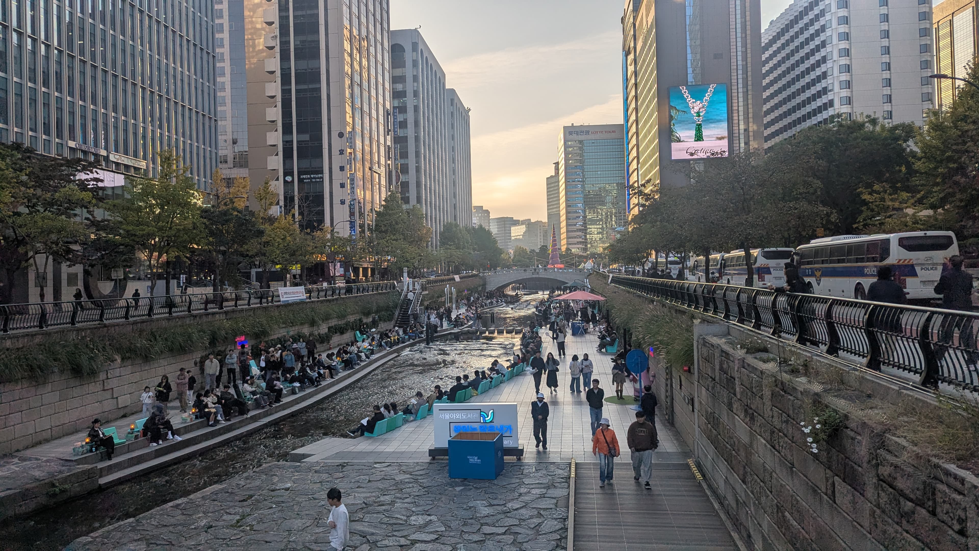 The Seoul Outdoor Library set up beside Cheonggyecheon stream — people reading and sitting along the daylit waterway in central Seoul.